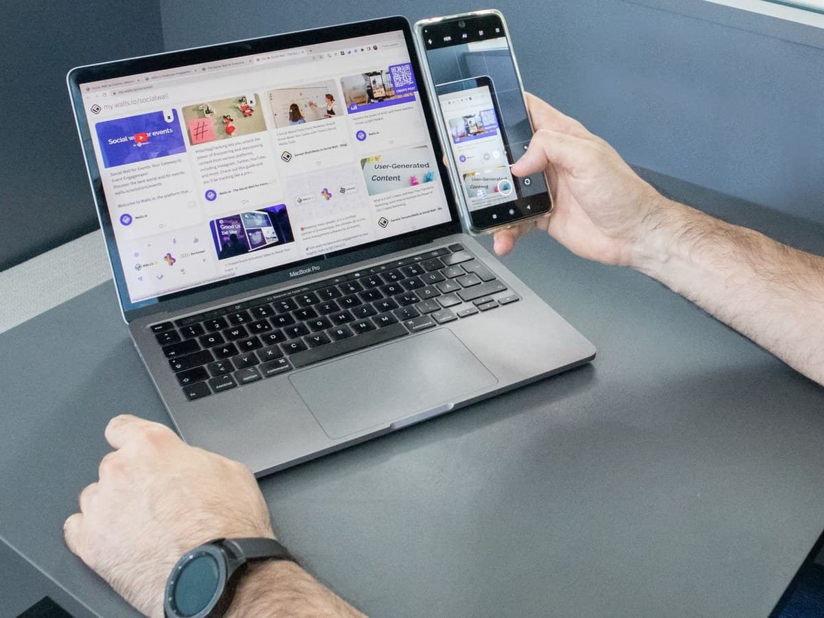 A laptop showing a website beside a phone displaying the same site as a mobile app, with a person's hands on both